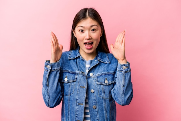Giovane donna cinese isolata su sfondo rosa che riceve una piacevole sorpresa eccitata e alza le mani