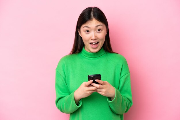 Giovane donna cinese isolata su sfondo rosa sorpresa e l'invio di un messaggio