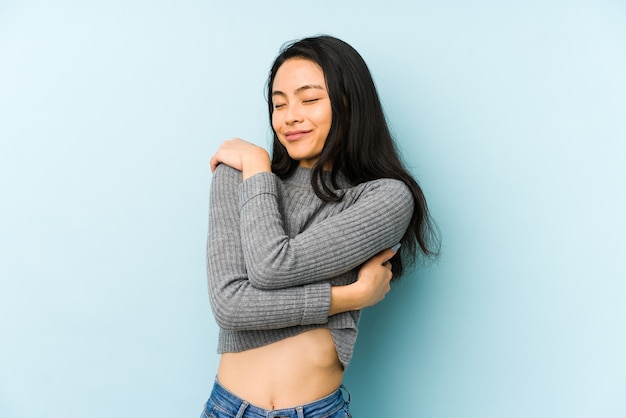 Giovane donna cinese isolata su uno sfondo blu abbracci, sorridendo spensierata e felice.