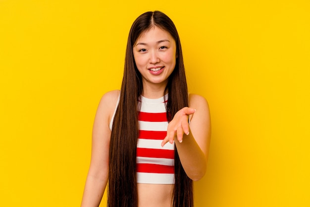 Giovane donna cinese isolata sul giallo che allunga la mano nel gesto di saluto.