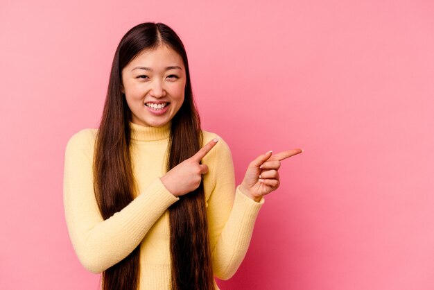 Giovane donna cinese isolata sul muro rosa che punta con gli indici a uno spazio di copia, esprimendo eccitazione e desiderio.