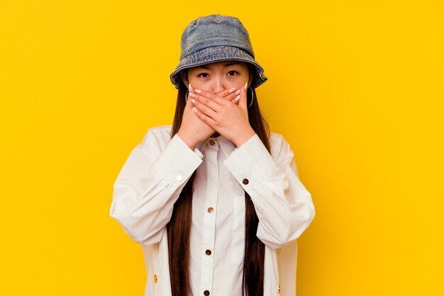 Giovane donna cinese isolata sulla bocca della copertura gialla con le mani che sembrano preoccupate.