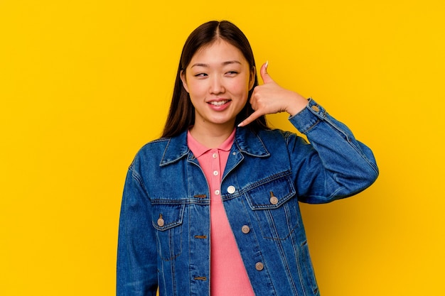 Giovane donna cinese isolata sulla parete gialla che mostra un gesto di chiamata di telefono cellulare con le dita.