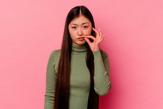 Giovane donna cinese isolata sulla parete rosa con le dita sulle labbra mantenendo un segreto