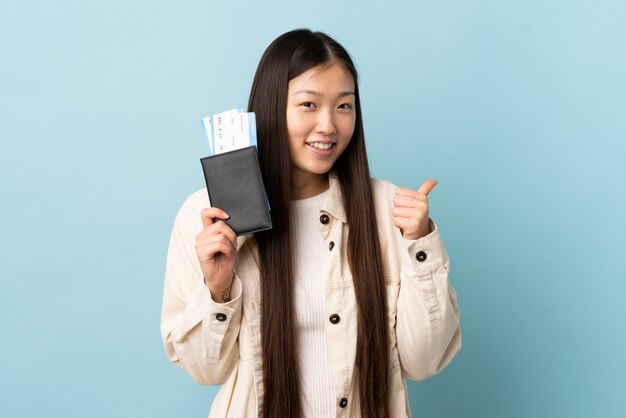 Giovane donna cinese sopra la parete isolata in vacanza che tiene un passaporto e un aereo con il pollice su