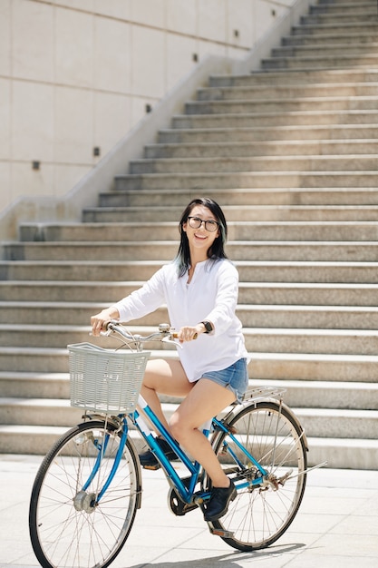 Giovane donna cinese sorridente adorabile che gode della guida sulla bicicletta in città il giorno soleggiato