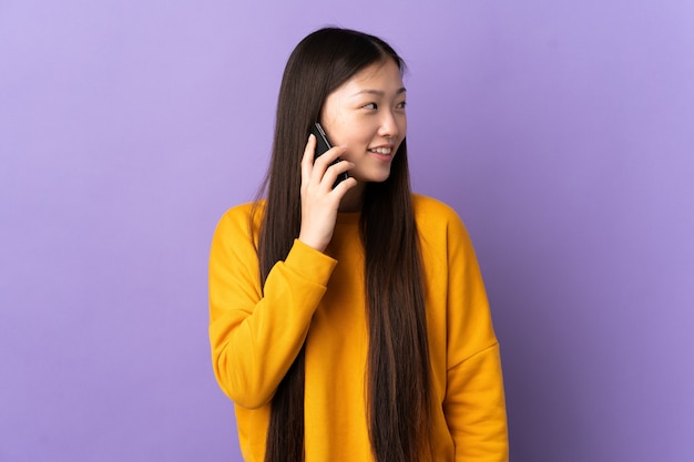 Giovane donna cinese sulla porpora isolata mantenendo una conversazione con il telefono cellulare con qualcuno