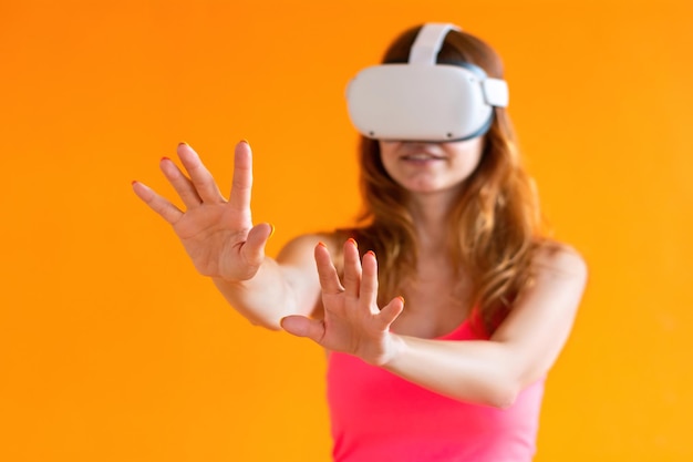 Giovane donna con auricolare realtà virtuale isolato su sfondo arancione Focus sulle mani