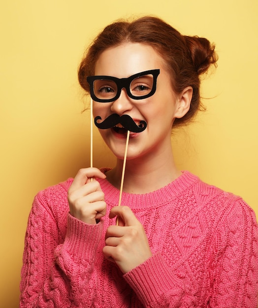 Giovane donna con baffi e occhiali finti su backgro giallo