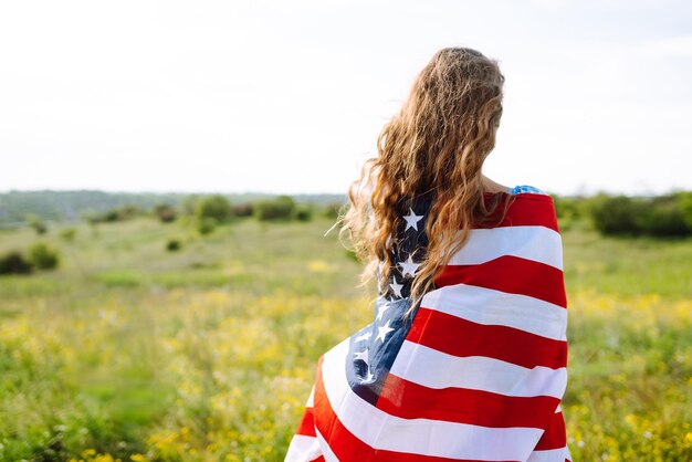 Giovane donna con bandiera americana degli Stati Uniti sul prato fiorito Festa dell'Indipendenza 4 luglio