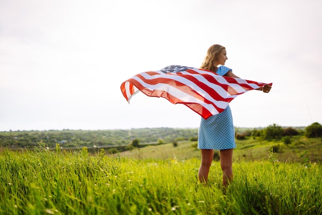 Giovane donna con bandiera americana degli Stati Uniti sul prato fiorito Festa dell'Indipendenza 4 luglio