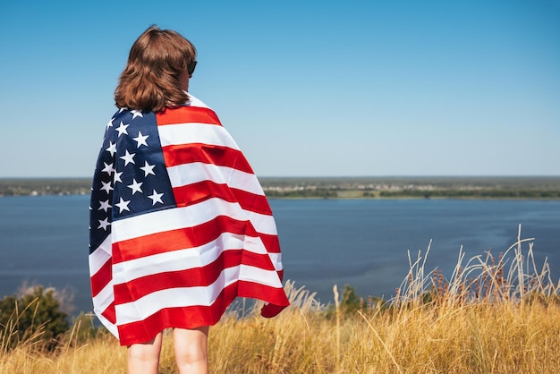 Giovane donna con bandiera americana in natura sullo sfondo del fiume in una giornata di sole