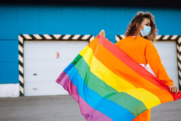 Giovane donna con bandiera LGBT e maschera protettiva