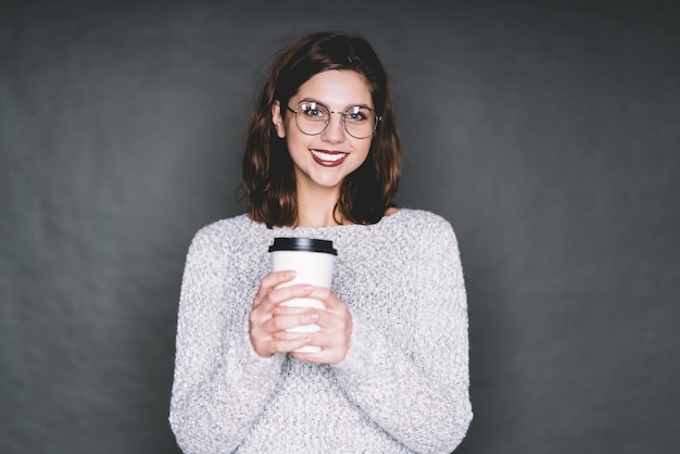 Giovane donna con bevanda sorridente per la fotocamera