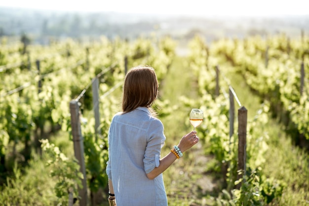 Giovane donna con bicchiere di vino in piedi sul bellissimo vigneto durante il tramonto