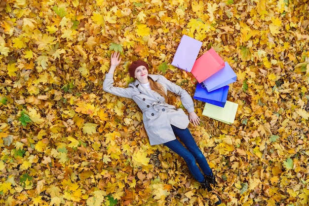 Giovane donna con borse della spesa colorate sdraiate sul fogliame Concetto di shopping e consumatore Vista dall'alto