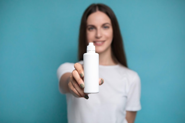 Giovane donna con bottiglia di soluzione per lenti su sfondo blu. Mock up di liquido per lenti