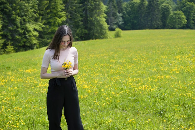 Giovane donna con bouquet di fiori di campo su un prato soleggiato.