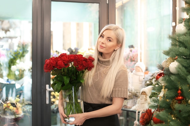 Giovane donna con bouquet di rose in piedi in negozio. Proprietario di una piccola attività