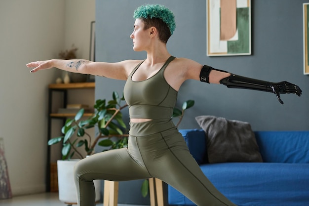 Giovane donna con braccio protesico che fa esercizi di stretching durante l'allenamento mattutino a casa