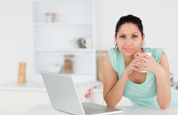 Giovane donna con caffè e laptop guardando alla telecamera