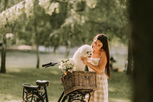 Giovane donna con cane bianco bichon frise nel cestino della bici elettrica