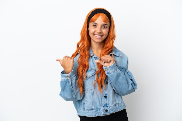 Giovane donna con capelli arancioni isolati su sfondo bianco che puntano al lato per presentare un prodotto