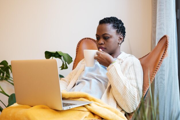 Giovane donna con capelli corti che lavora da casa con un caffè concentrato sul laptop Tecnologia di intrattenimento per telelavoro concettuale