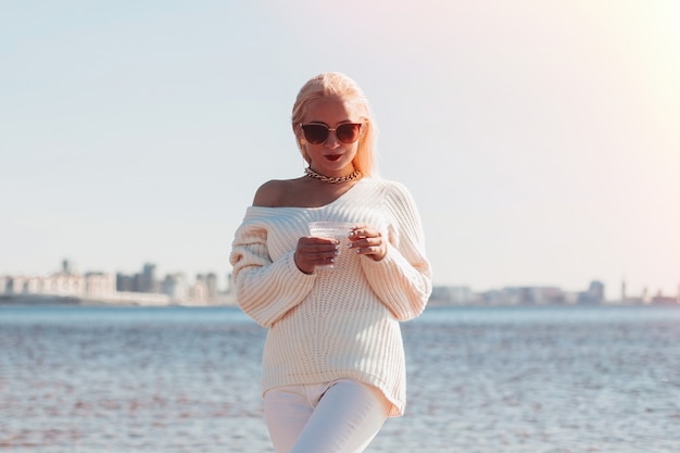 Giovane donna con capelli ondulati biondi che tiene un bicchiere di champagne sul mare