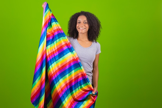 Giovane donna con capelli ricci che tiene bandiera arcobaleno isolato sfondo verde Concetto LGBT