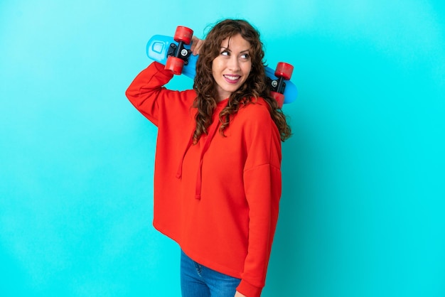 Giovane donna con capelli ricci isolata su fondo blu con un pattino con espressione felice