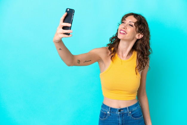 Giovane donna con capelli ricci isolata su sfondo blu che fa un selfie