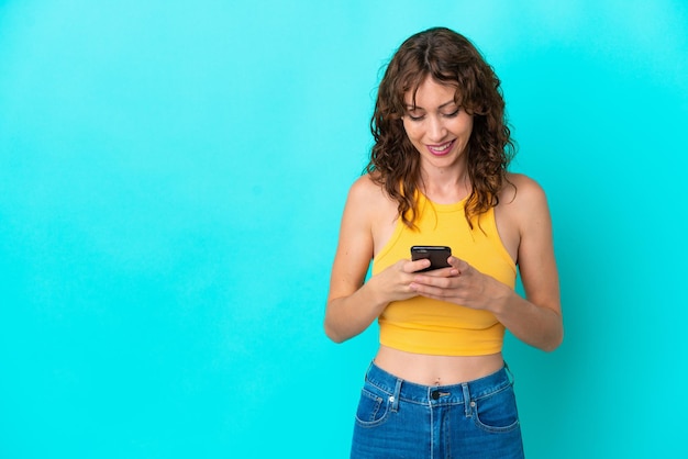 Giovane donna con capelli ricci isolata su sfondo blu che invia un messaggio con il cellulare