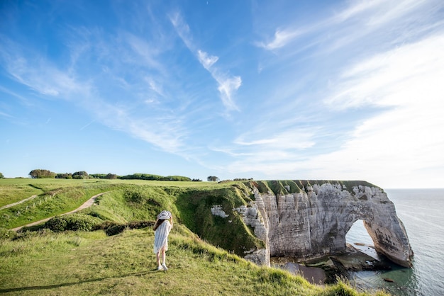 Giovane donna con cappello a strisce e maglione che gode di una splendida vista sulla famosa costa rocciosa vicino alla città di Etretat in Francia