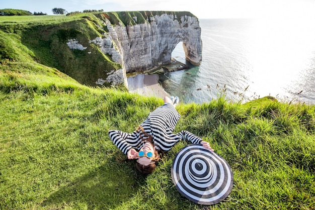 Giovane donna con cappello a strisce e maglione che gode di una splendida vista sulla famosa costa rocciosa vicino alla città di Etretat in Francia