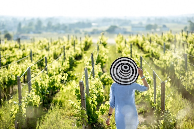 Giovane donna con cappello a strisce godendo di una splendida vista del tramonto sul vigneto nella regione di Bordeaux in Francia