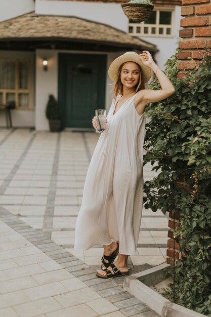 Giovane donna con cappello che beve limonata fredda nel giardino del resort