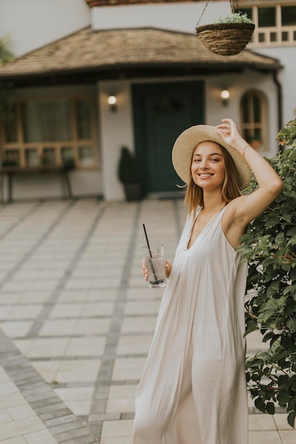 Giovane donna con cappello che beve limonata fredda nel giardino del resort