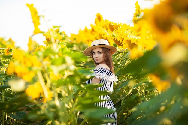 Giovane donna con cappello che si gode l'estate nel campo di girasoli al tramonto