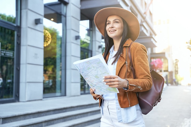 Giovane donna con cappello che usa la mappa mentre si cammina all'aperto