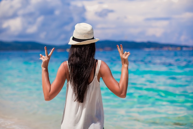 Giovane donna con cappello con le mani sollevate in spiaggia perfetta