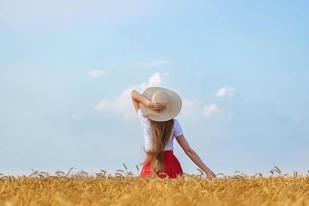 Giovane donna con cappello sul campo di grano e lo sfondo del cielo. La libertà rilassa una naturalezza