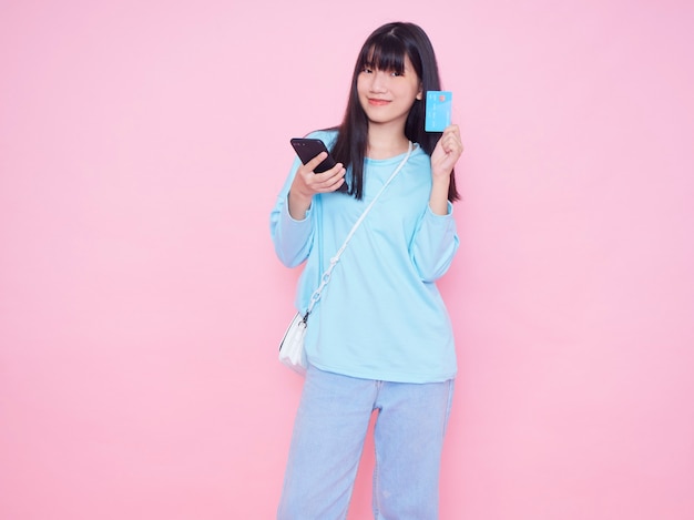Giovane donna con carta di credito e smartphone sulla parete rosa. Acquisti online