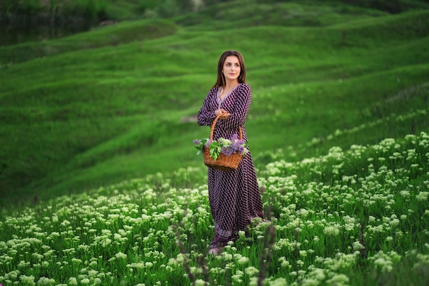 Giovane donna con cesto di vimini pieno di fiori in campo