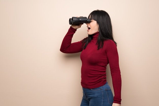 Giovane donna con collo alto rosso e guardando in lontananza con il binocolo