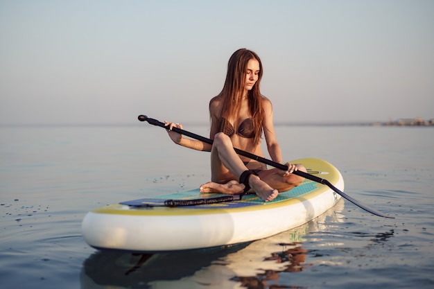 Giovane donna con corpo in forma sexy in posa sulla tavola da paddle in mare