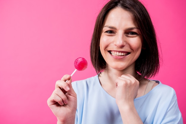 Giovane donna con denti sensibili che mangia lecca-lecca dolce su sfondo a colori