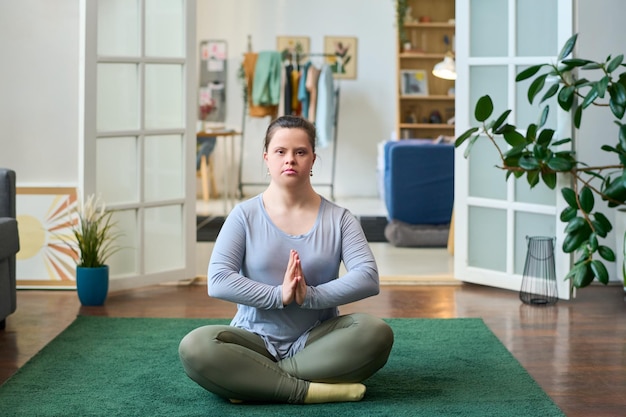 Giovane donna con disabilità seduta in posa di loto mentre pratica yoga