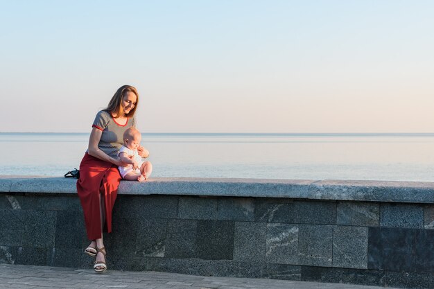 Giovane donna con fare da baby-sitter sul mare al tramonto. Felice maternità e armonia