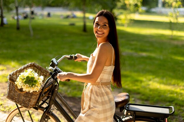 Giovane donna con fiori nel cestino della bici elettrica